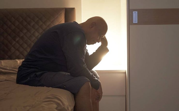 Man sitting on the edge of his bed unable to sleep