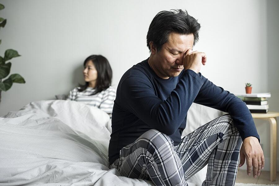 Man sitting on his bed with his hand on his forehead