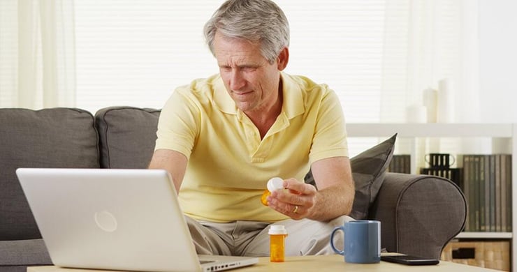 Man holding a prescription pill bottle and looking at a laptop